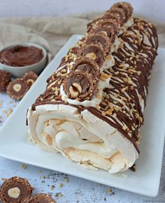 a white plate topped with an ice cream roll covered in chocolate and pretzels