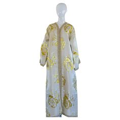 Vintage elegant Moroccan caftan white and gold lame metallic floral brocade, circa 1970s. It’s crafted in Morocco and tailored for a relaxed fit with wide sleeves This long vintage maxi dress kaftan is embroidered and embellished entirely by hand. One of a kind evening Moroccan Middle Eastern gown. The kaftan features a traditional neckline, embellished sleeves. It is a slip on, the button does not open. In Morocco, fashion preserves its traditional style inherited from great civilizations that Gold Embroidered Floor-length Thobe, Embroidered Gold Floor-length Thobe, Gold Embroidered Floor-length Abaya, Gold Floor-length Abaya With Gold Embroidery, Festive Gold Maxi Length Thobe, Elegant Gold Long Sleeve Agbada, Gold Long Sleeve Agbada For Eid, Festive Gold Long Thobe, Festive Gold Thobe With Gold Embroidery