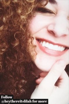 a woman with curly hair smiling and holding her hand to her face while looking at the camera