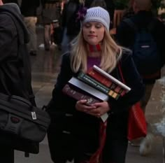 a woman is walking down the street carrying books