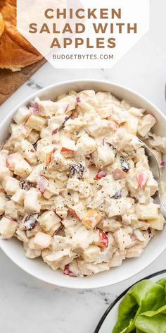 chicken salad with apples in a white bowl on top of a table next to bread