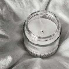 a white candle sitting on top of a bed next to a glass jar filled with liquid