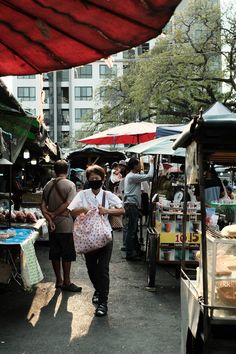 people are shopping at an outdoor market with umbrellas and food stalls in the background