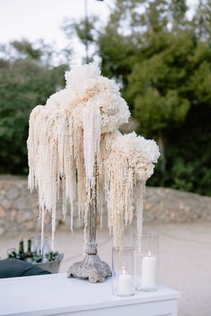 a tall vase filled with white flowers next to two candles on top of a table