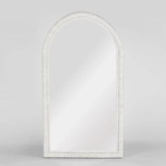 an arched white mirror with beading around the edges