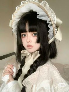 a doll with long black hair wearing a white dress and bonnet on top of a bed