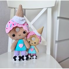 two small crocheted dolls standing next to each other on a white chair,