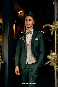 a man wearing a green suit and bow tie standing in front of a door with his hands in his pockets