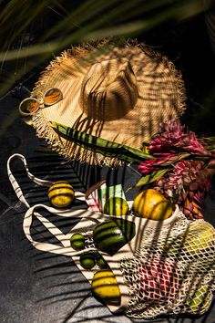 two straw hats and some fruit in a basket on top of a black surface with long shadows