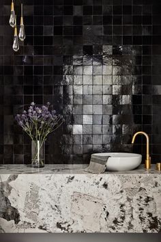 a black and white tiled bathroom with gold faucet, marble counter top and sink