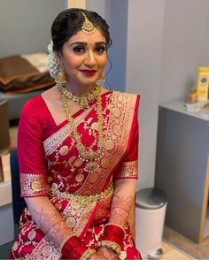 a woman in a red and gold bridal outfit sitting on a chair with her hands together