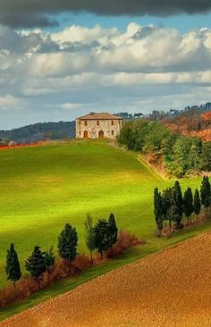 an old farm house sits on top of a green hill with trees in the foreground