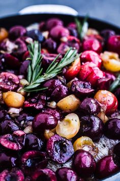 a pan filled with cooked cherries and rosemary garnish on top of it