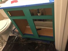 an unfinished bathroom cabinet being painted green and blue with the toilet in the back ground