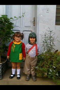 two young children standing next to each other in front of a white door with potted plants