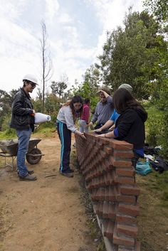 a group of people standing next to each other near a brick wall on a dirt road