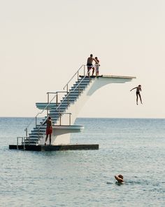 three people are diving into the ocean from a floating platform