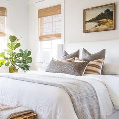 a bed with white linens and pillows in a bedroom next to two large windows