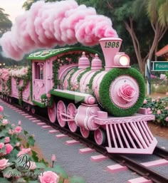 a pink and green train with flowers on it's side is going down the track