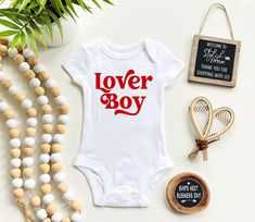 a white bodysuit with the words lover boy on it next to tennis rackets