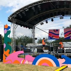 the stage is set up for an outdoor music festival with colorful art on it's sides