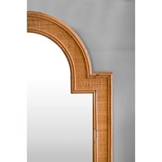 an arched wooden mirror frame with wicker design on the top and bottom half, against a gray wall