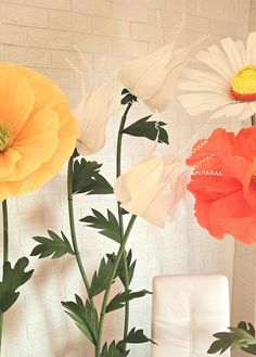 three large flowers are in a vase on the table next to a white chair and brick wall