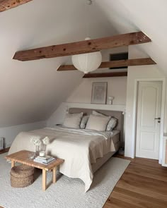 an attic bedroom with white walls and wood beams on the ceiling, along with a large bed