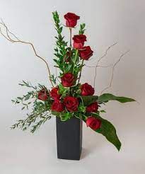 a black vase filled with red roses and greenery