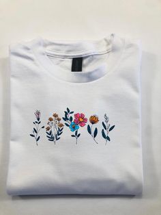 a white t - shirt with colorful flowers on the front and back, sitting on a table