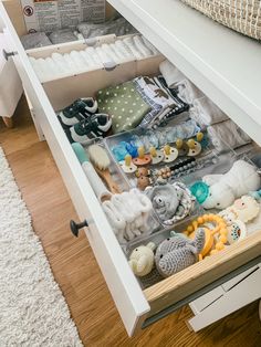 an open drawer filled with baby items on top of a wooden floor next to a bed