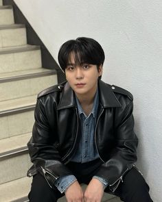 a young man sitting on the steps wearing a black leather jacket