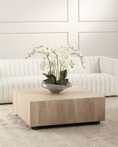 a living room with white couches and flowers in a vase on the coffee table