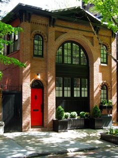 a red door is in front of a brick building with black shutters and windows