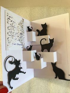 an open book with black cats on it and paper cut out to look like they are playing