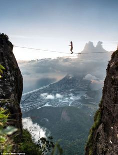 a man walking across a tight rope over a valley below the clouds on top of a mountain