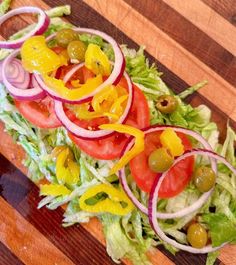 a salad with tomatoes, onions and olives on a wooden cutting board next to a knife