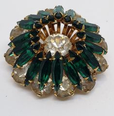 This brooch has two layers. The large round rhinestones make the outer lower level while the beautiful deep emerald green navettes cascade downward from the second level. In the center is an extra large rhinestone crystal. All of the stones are prong set. The pictures don't catch the real beauty, it's much more brilliant in person. It's a perfect special touch for that special outfit! It is 1 1/2 in. in diameter and 3/4 in high. It is in excellent vintage condition. ENJOY Thank you so much for l Green Round Brooches For Wedding, Green Round Wedding Brooches, Green Round Brooch Jewelry, Retro Green Brooch Jewelry, Vintage Green Flower Brooches, Vintage Multi-stone Brooches For Formal Occasions, Antique Pins, Vintage Yellow Gold Multi-stone Brooches, Flower Circle