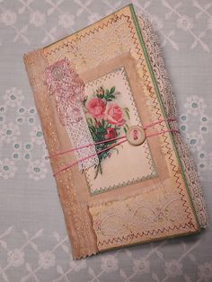 an old book with lace and flowers on it sitting on top of a tablecloth