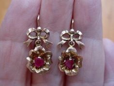 "These antique earrings are hard to date. The bow motif was popular in the Georgian era and again in the late Victorian/Edwardian era. I am guessing the latter. They have bow shaped tops and a flower dangle base. Each flower has a .30 carat natural ruby. These earrings are small and measure about 1\" from the wire tops. One earring is missing its small wire catch. The piece is there and can be soldered back into place or wear them as is. I will include a plastic stopper to use so not to lose the Yellow Gold Bow Earrings For Wedding, Victorian Screw Back Earrings For Formal Occasions, Victorian 14k Gold Earrings, Victorian 14k Gold Earrings For Anniversary, Classic Bow Earrings For Anniversary, Vintage 14k Gold Earrings, Vintage 14k Gold Wedding Earrings, Vintage 14k Gold Screw Back Earrings, Vintage Wedding Jewelry With Bow Detail