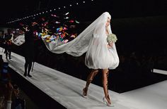 a woman walking down a runway with a veil over her head