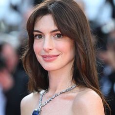 a woman with long hair wearing a blue dress and smiling at the camera while standing in front of photographers