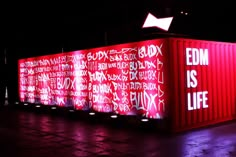 a large red container with writing on it in the middle of a parking lot at night