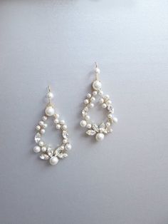 two pairs of pearl and crystal earrings on top of a white surface with an object in the background