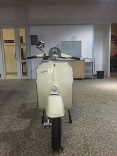 a white scooter is parked in an empty room with no one on it