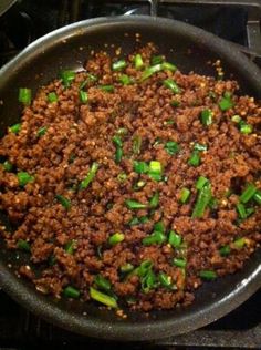 a pan filled with meat and green onions on top of a stovetop next to an oven