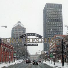 a street with cars driving under a welcome sign in the middle of it's snowing day