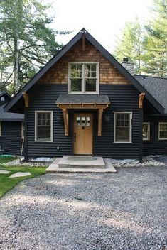 a black house in the woods with gravel driveway