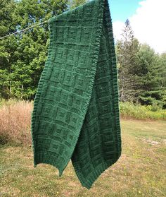 a green knitted blanket hanging from a clothes line in the grass near some trees