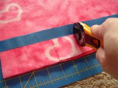 someone cutting fabric with scissors on top of a pink and blue piece of cloth that has the word love written on it